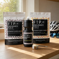 FTP Power Fluids Rotation Pack on a kitchen counter — two 900g pouches, black 710ml bottle, scoop of drink mix and cycling helmet