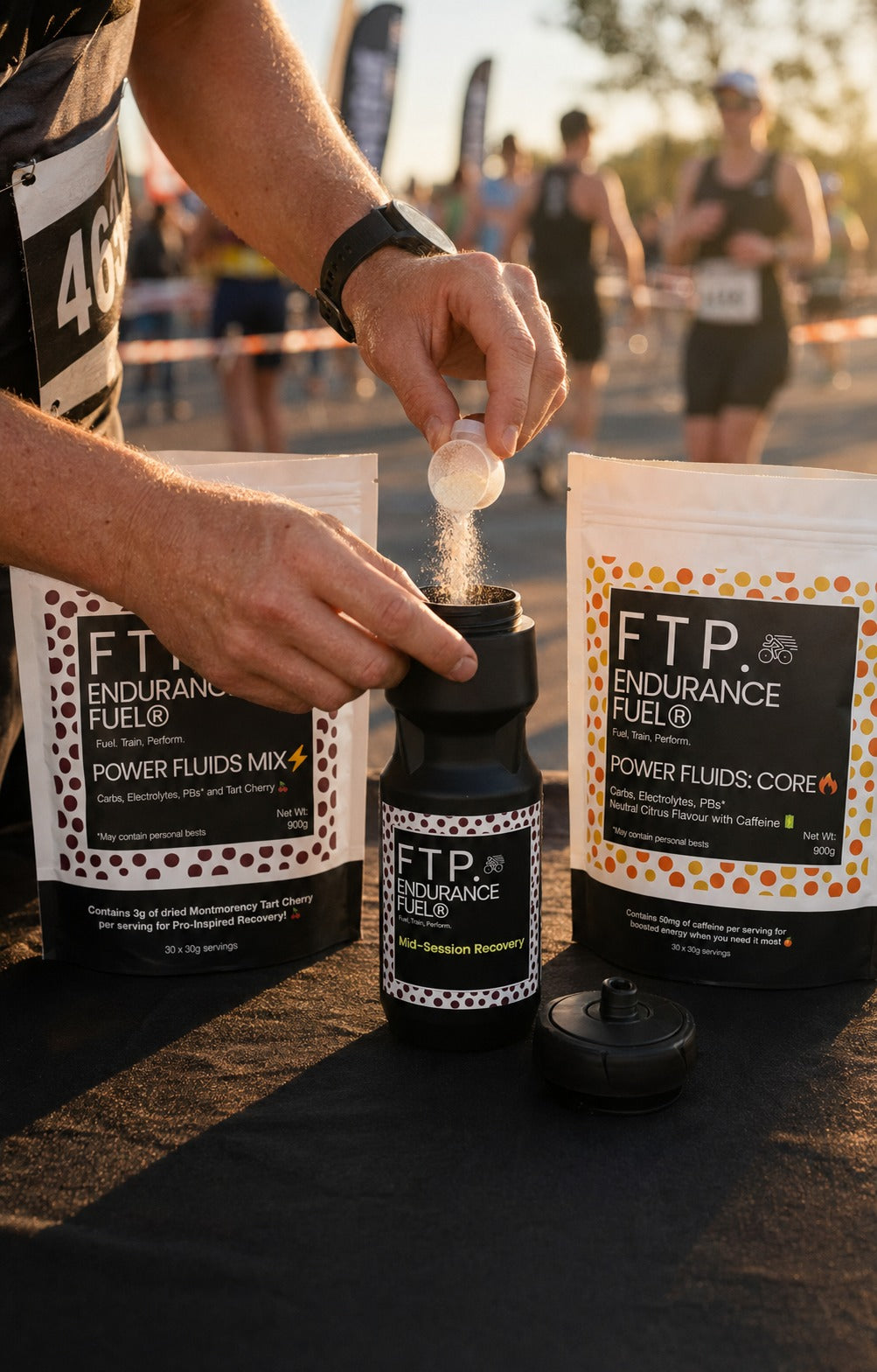 Athlete scooping FTP Power Fluids drink mix into a black 710ml FTP bottle at a race aid station, Tart Cherry and Core 900g pouches behind