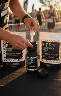 Athlete scooping FTP Power Fluids Tart Cherry drink mix into a black 710ml FTP bottle at a race aid station